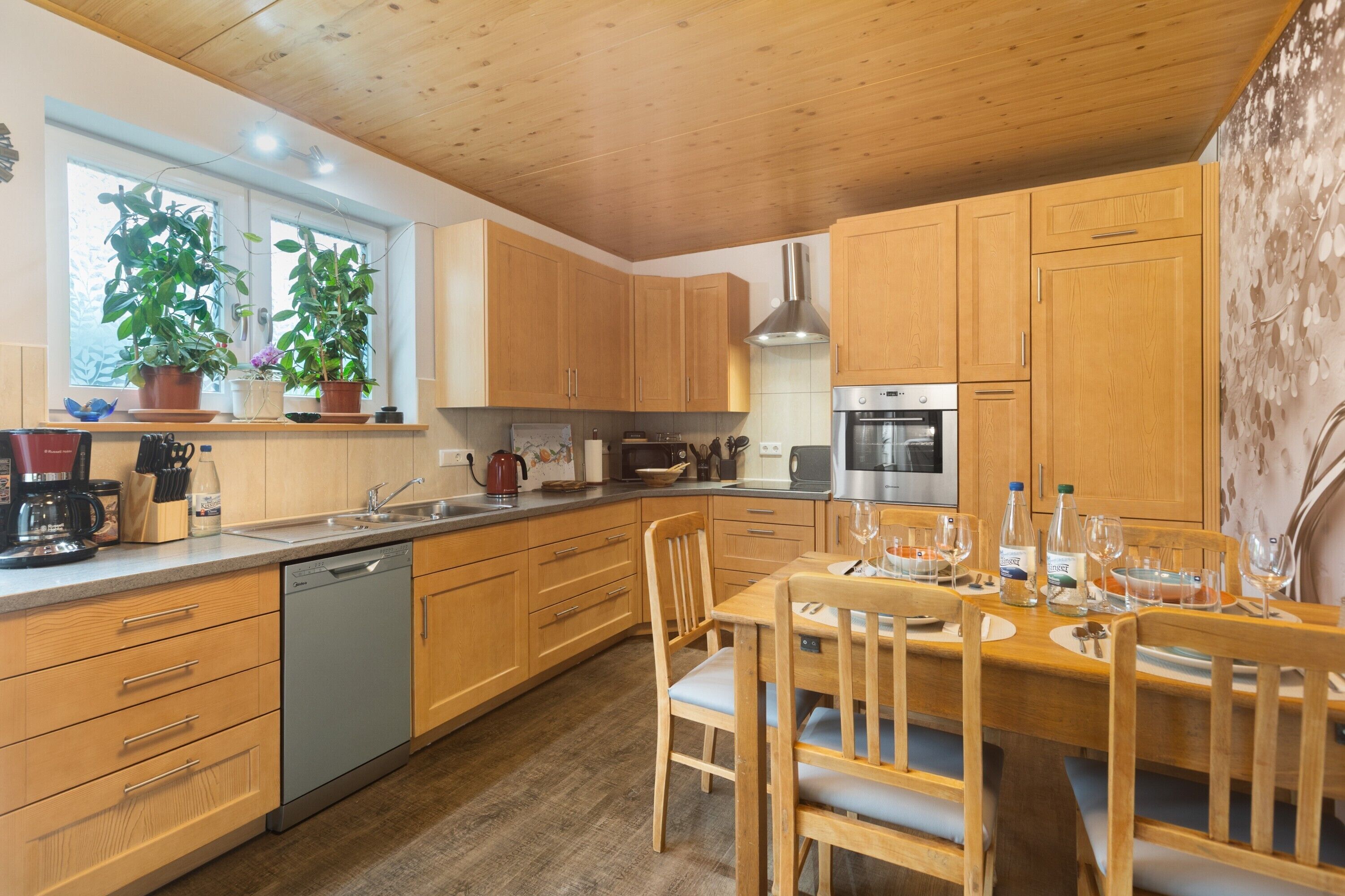 A modern kitchen with wooden cabinets, a dishwasher, a stove, and a dining table set for four.