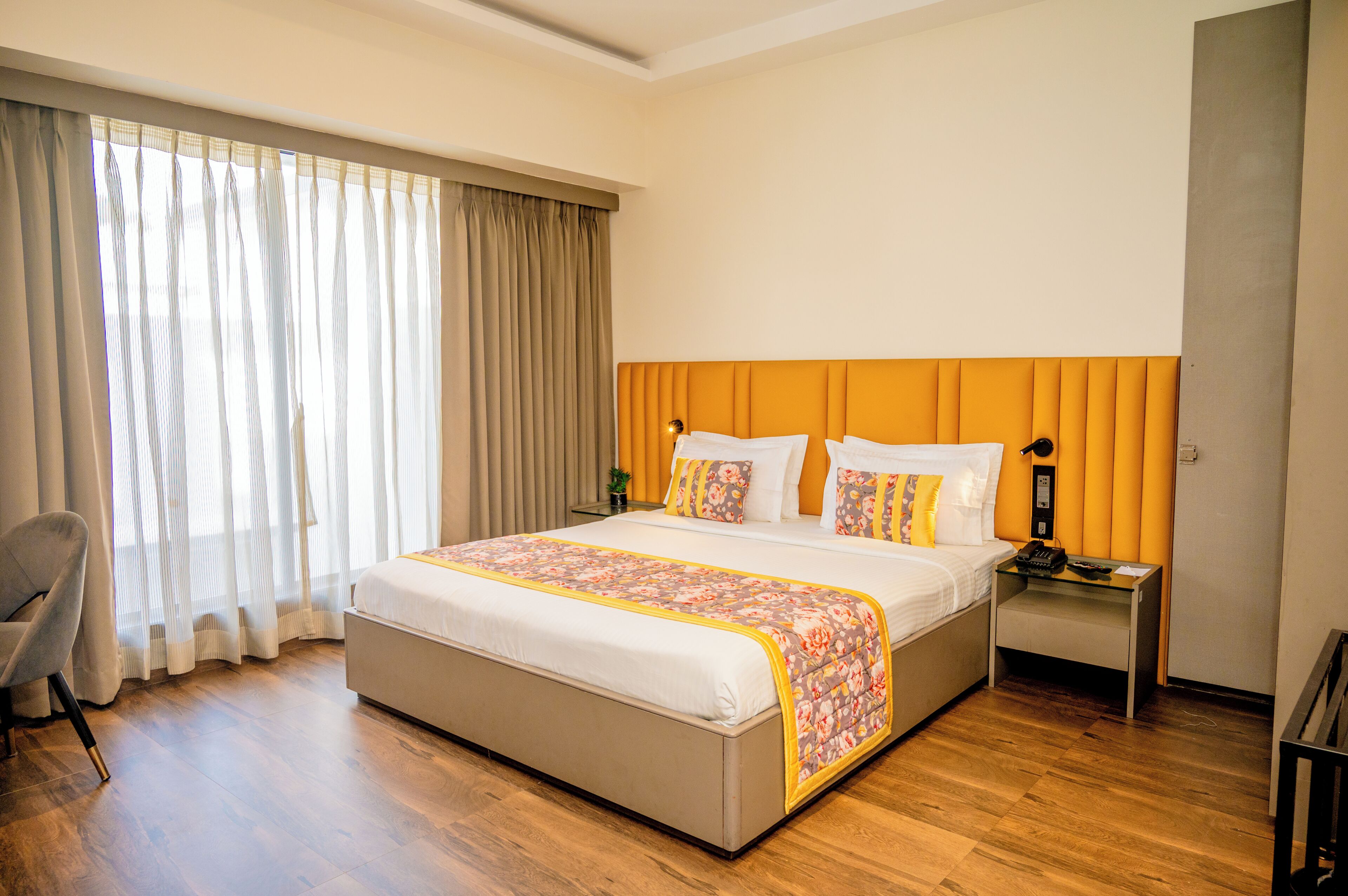 A hotel room with a large bed, a bedside table, a chair, and a window with curtains.