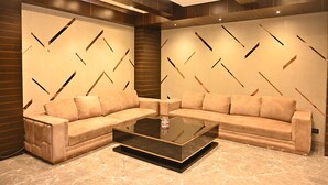 A modern living room with a sectional sofa, a glass coffee table, and a geometric patterned wall. - Urvi Banquets & Guest House  (Bidhannagar)