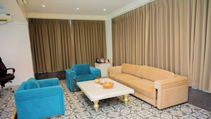 A living room with a beige sofa, two blue armchairs, and a coffee table with a bowl of fruit. - Urvi Banquets & Guest House  (Bidhannagar)