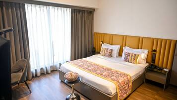 A hotel room with a large bed, a bedside table, a chair, and a view of the outdoors through the window.