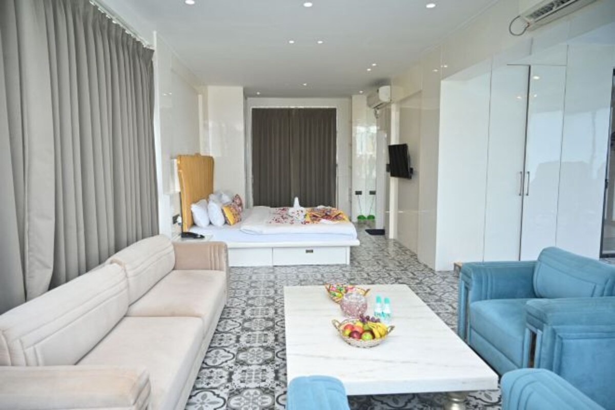 Ett modernt hotellrum med en säng, en soffa, ett soffbord med frukt och en garderob.