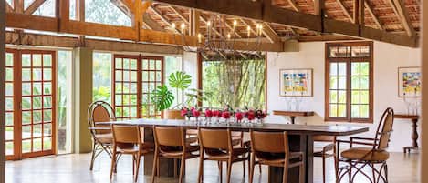 A spacious dining area with a large wooden table and chairs, surrounded by large windows and doors.