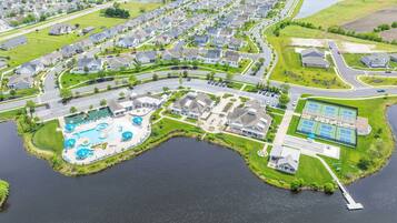 An aerial view of a residential area with a large swimming pool, tennis courts, and a dock.