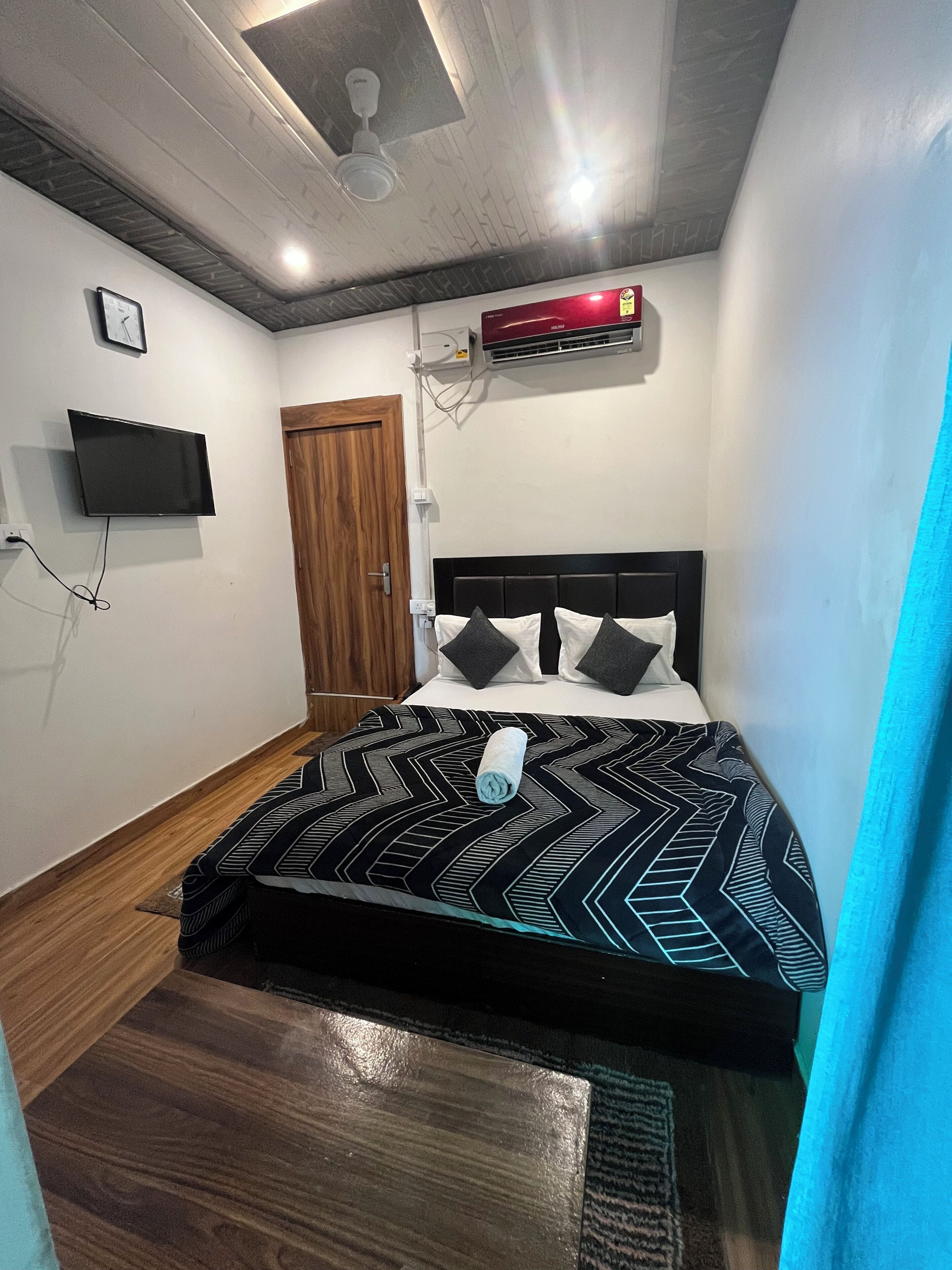 A bedroom with a bed, a television mounted on the wall, a ceiling fan, and an air conditioning unit.