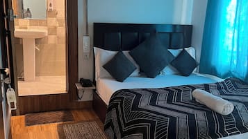 A bedroom with a bed, a bedside table, a nightstand, a mirror, a sink, and a shower area.