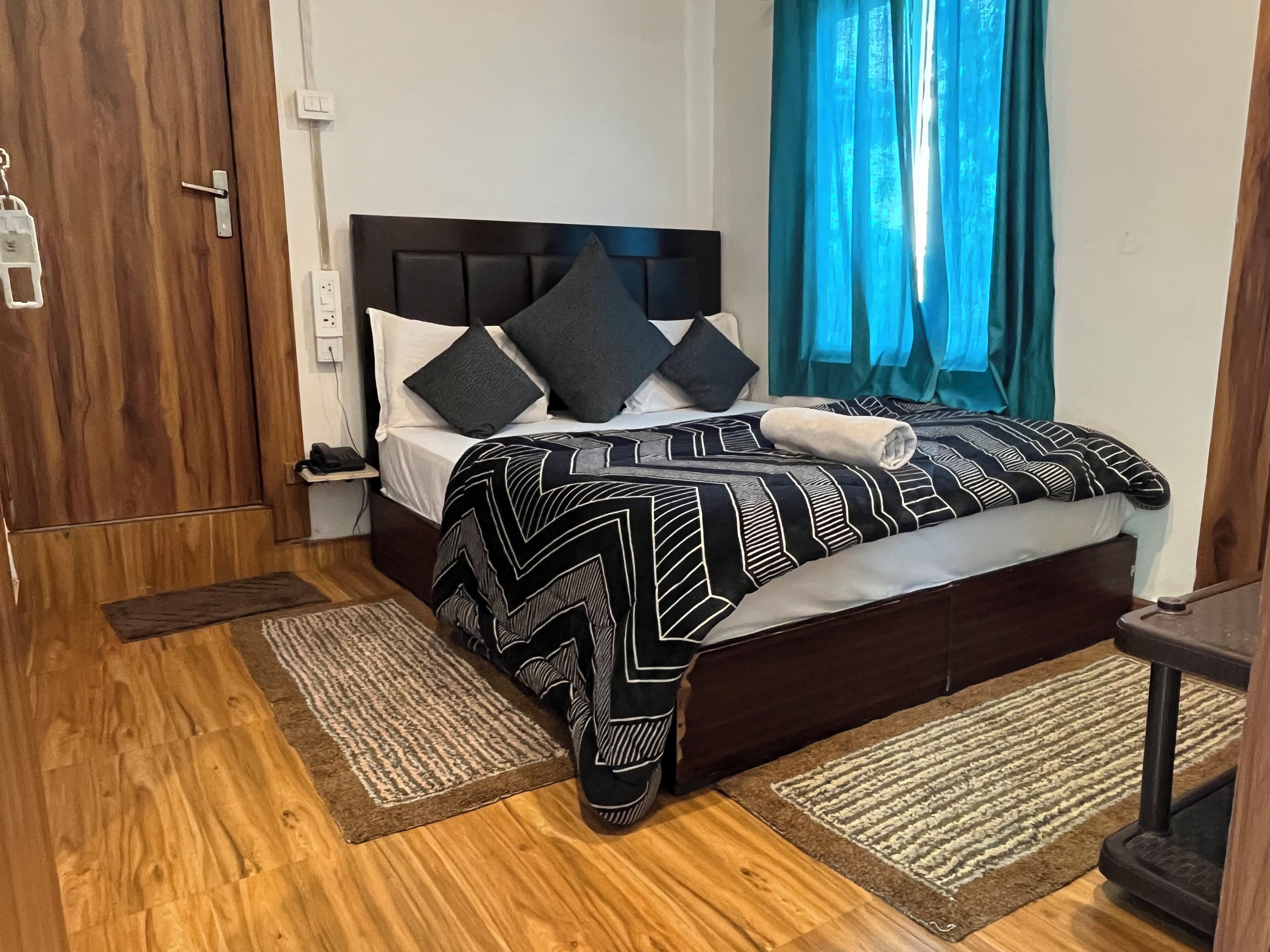 A neatly made bed with a patterned bedspread, a bedside table with a lamp, and a wooden floor.