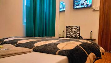 A bedroom with a bed, a TV mounted on the wall, a window with curtains, and a wooden floor.