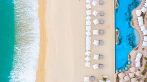 An aerial view of a beach resort with a swimming pool, beach umbrellas, and lounge chairs.