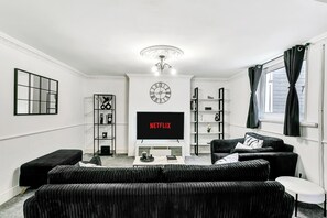 Een moderne woonkamer met een flatscreen televisie, zwarte banken, een bijzettafeltje en een boekenkast.