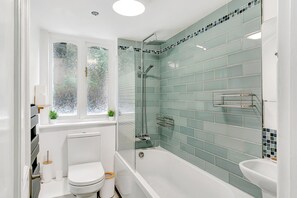 Een badkamer met een bad, toilet en een raam met gezandstraald glas.
