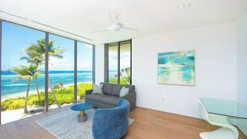 A modern living room with a large window overlooking a beach, a ceiling fan, and a glass table.