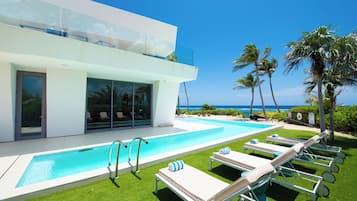 Un espace piscine moderne offrant une vue dégagée sur l’océan, avec une piscine et des chaises longues.