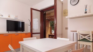 Una cocina moderna con televisor de pantalla plana, gabinetes color naranja, una mesa de comedor blanca y una puerta de madera que da a un espacio exterior.