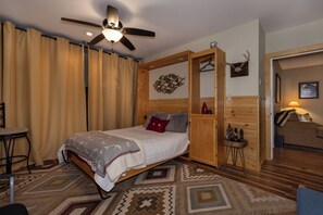 Ein Schlafzimmer mit einem Bett, einem Deckenventilator, einem Holzschrank, einem kleinen Tisch und einer Couch.
