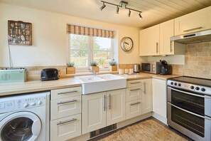 A compact kitchen with a washing machine, a sink, a stove, and a microwave. - Host Stay Pebble Cottage (Norwich)
