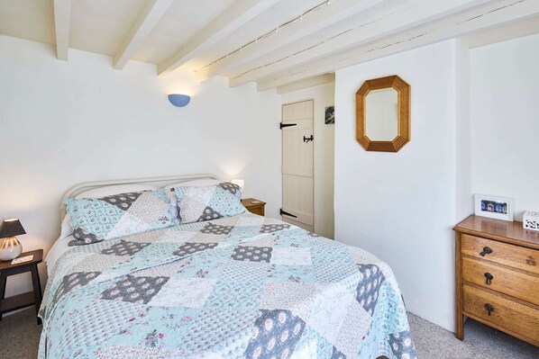 A bedroom with a bed, a wooden dresser, a mirror, and a door. - Host Stay Pebble Cottage (Norwich)