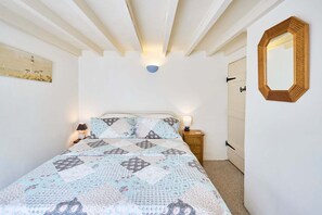A bedroom with a bed, a nightstand, a wall-mounted mirror, and a door. - Host Stay Pebble Cottage (Norwich)