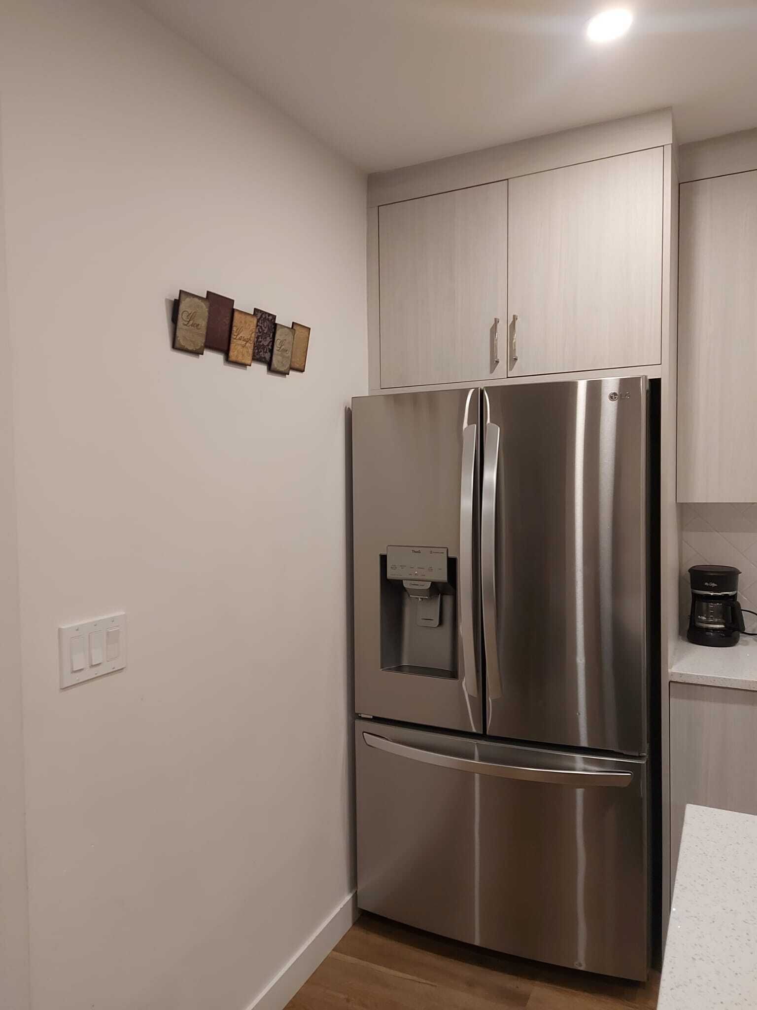 A stainless steel refrigerator with a water dispenser, a coffee maker, and wooden wall decor.