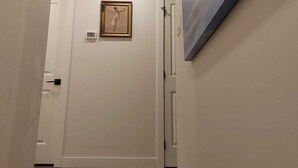 A hallway with a wooden staircase, white walls, a framed picture, and a painting. - Cozy Haven in Glenbrook close to downtown (Calgary)