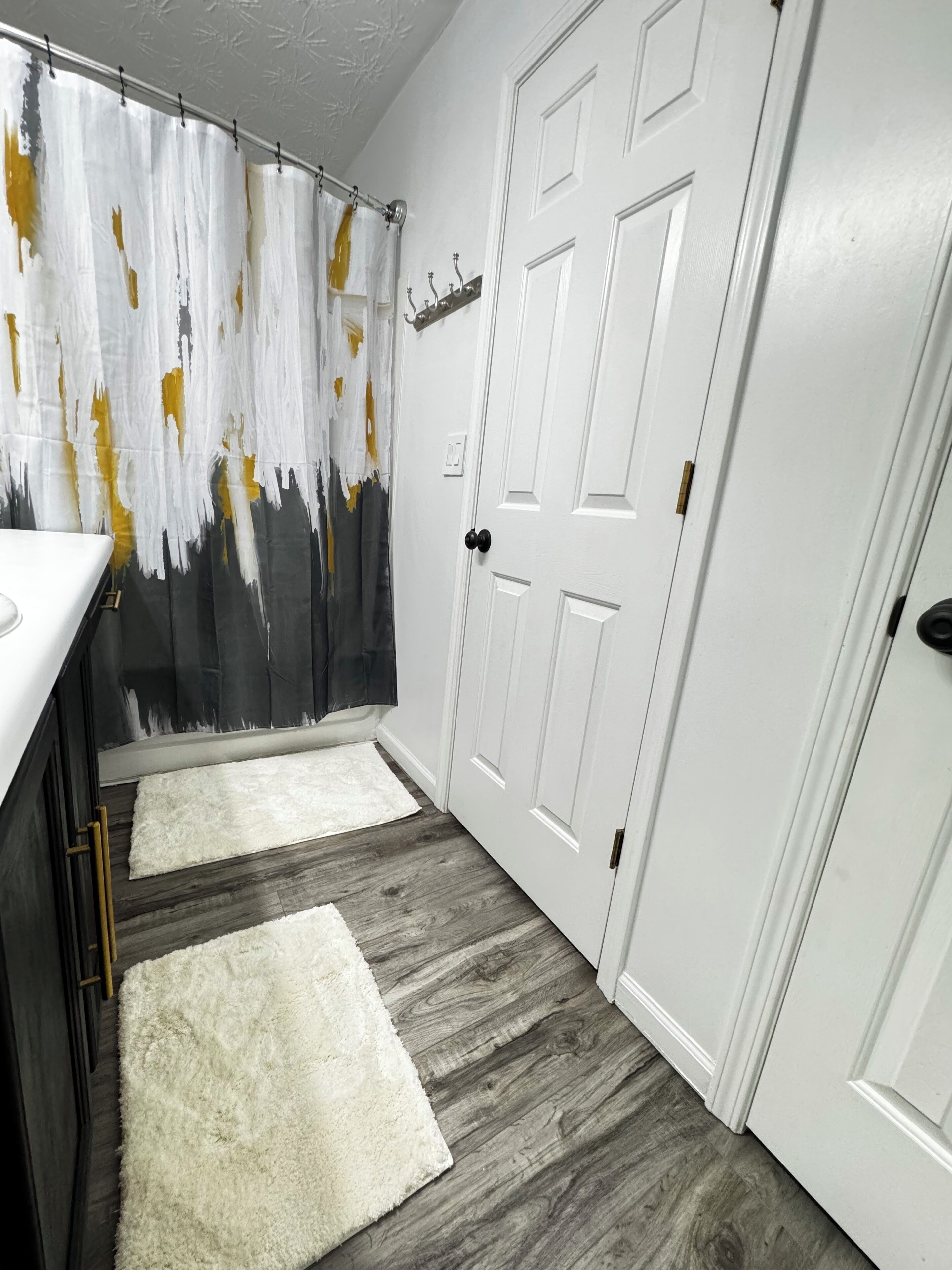 A hallway with a white door, a white wall with a white and yellow abstract painting, and a wooden floor.