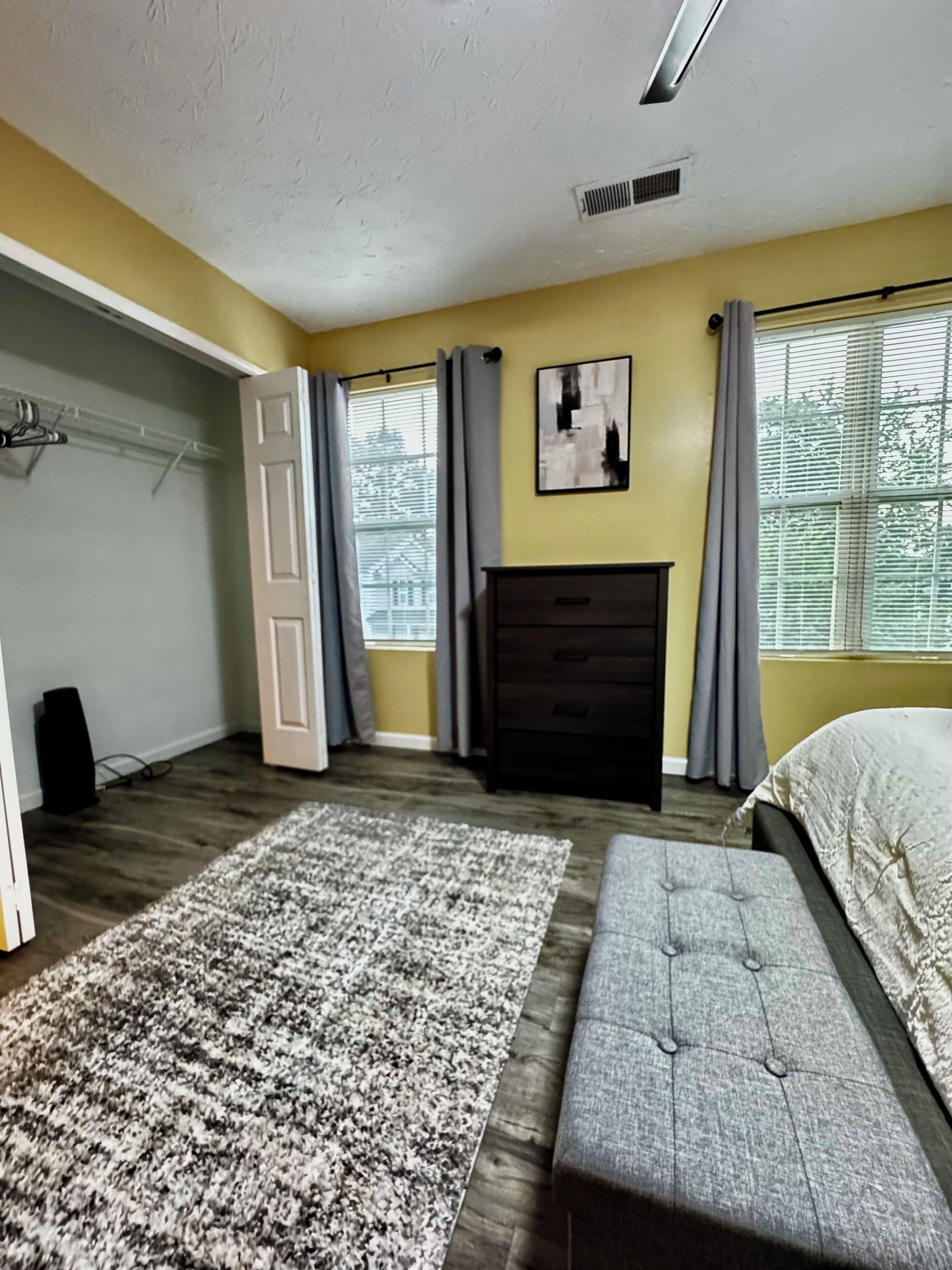 Une chambre à coucher avec un lit, une commode, un tapis et une fenêtre avec des rideaux.