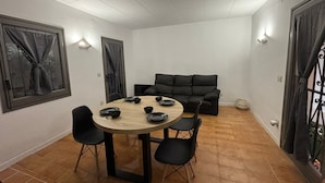 A dining area with a round table, four chairs, a sofa, and two windows with curtains. - Casita moderna vacacional en roses (roses)