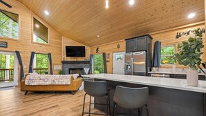 A modern cabin interior with a wooden interior, a kitchen area, a fireplace, and a large window overlooking greenery. - Prized Gem - Spa-like Retreat in the Heart of Nature (Cleveland)