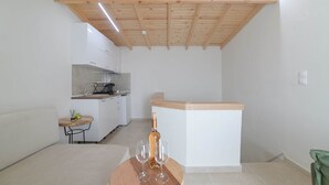A compact kitchen with white cabinets, a wooden ceiling, and a small dining area with a round table and two glasses. - Chalkidiki s Seaview Escape - Cozy Summer Getaway (Nea Propontida)