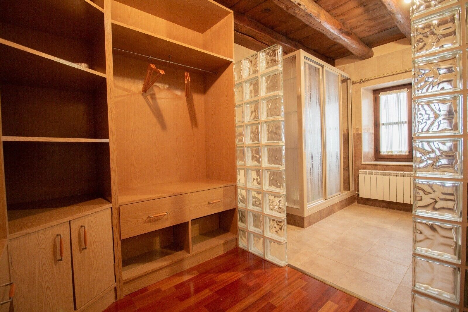 A room with wooden cabinets, a glass block partition, and a window with blinds.