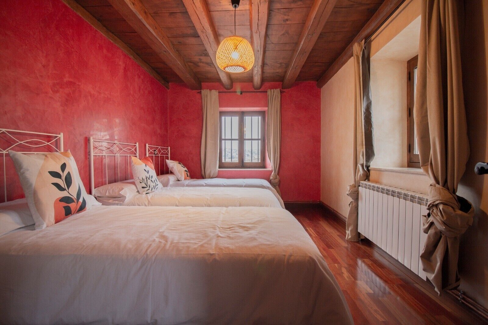 Una habitación con dos camas, una ventana con cortinas, un radiador y una lámpara colgante.