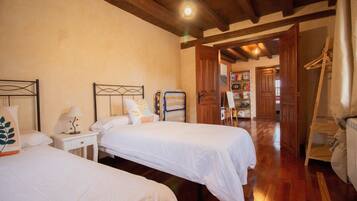A room with two beds, wooden flooring, a wooden ceiling, and a view of a hallway with a door leading outside.