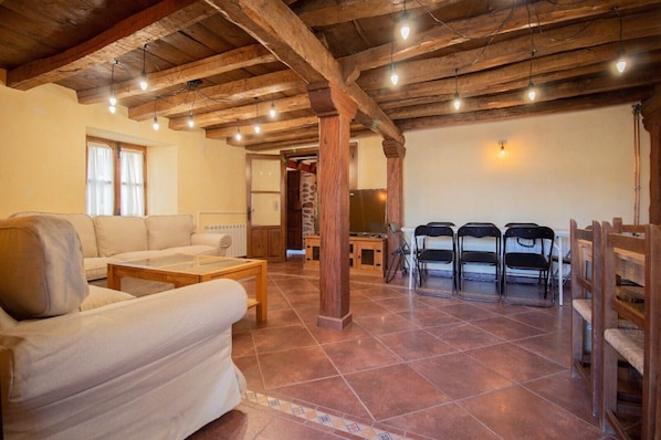 Un salon avec un canapé, une table basse et des fauteuils, des poutres en bois au plafond et un téléviseur à l’arrière-plan.