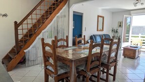A dining area with a wooden table and chairs, a staircase, and a view of the outside. - Quiet house, large south-facing garden (Crozon)