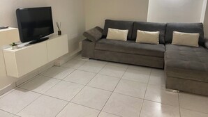 A living room with a flat-screen TV on a white cabinet, a grey sofa with cushions, and a tiled floor. - HISTORIC CITY STUDIO (Vence)