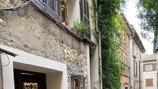 A narrow street with a stone building featuring a wooden door with decorative glass panels. - HISTORIC CITY STUDIO (Vence)