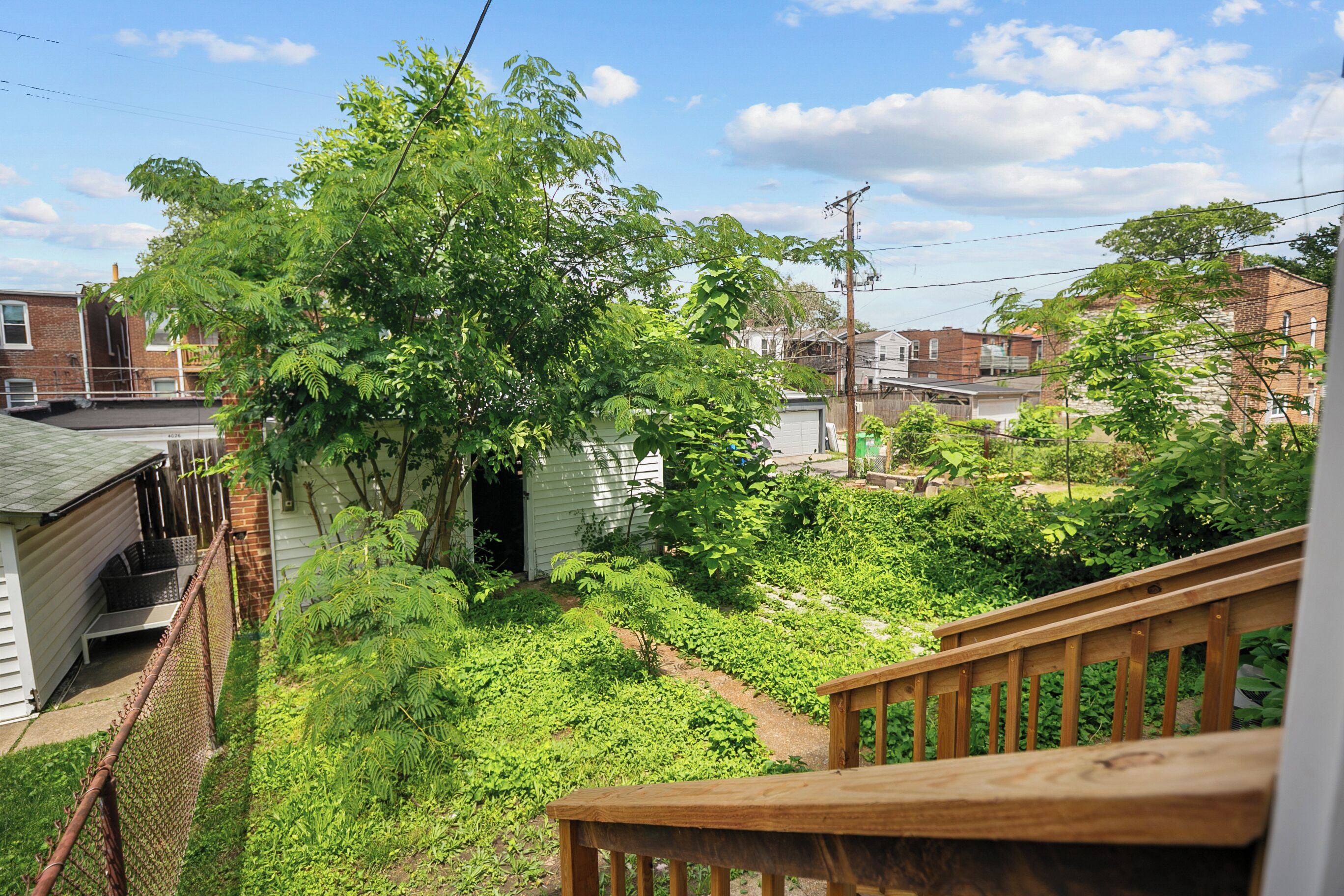 A residential backyard with a wooden deck, a small garden, and a white house.
