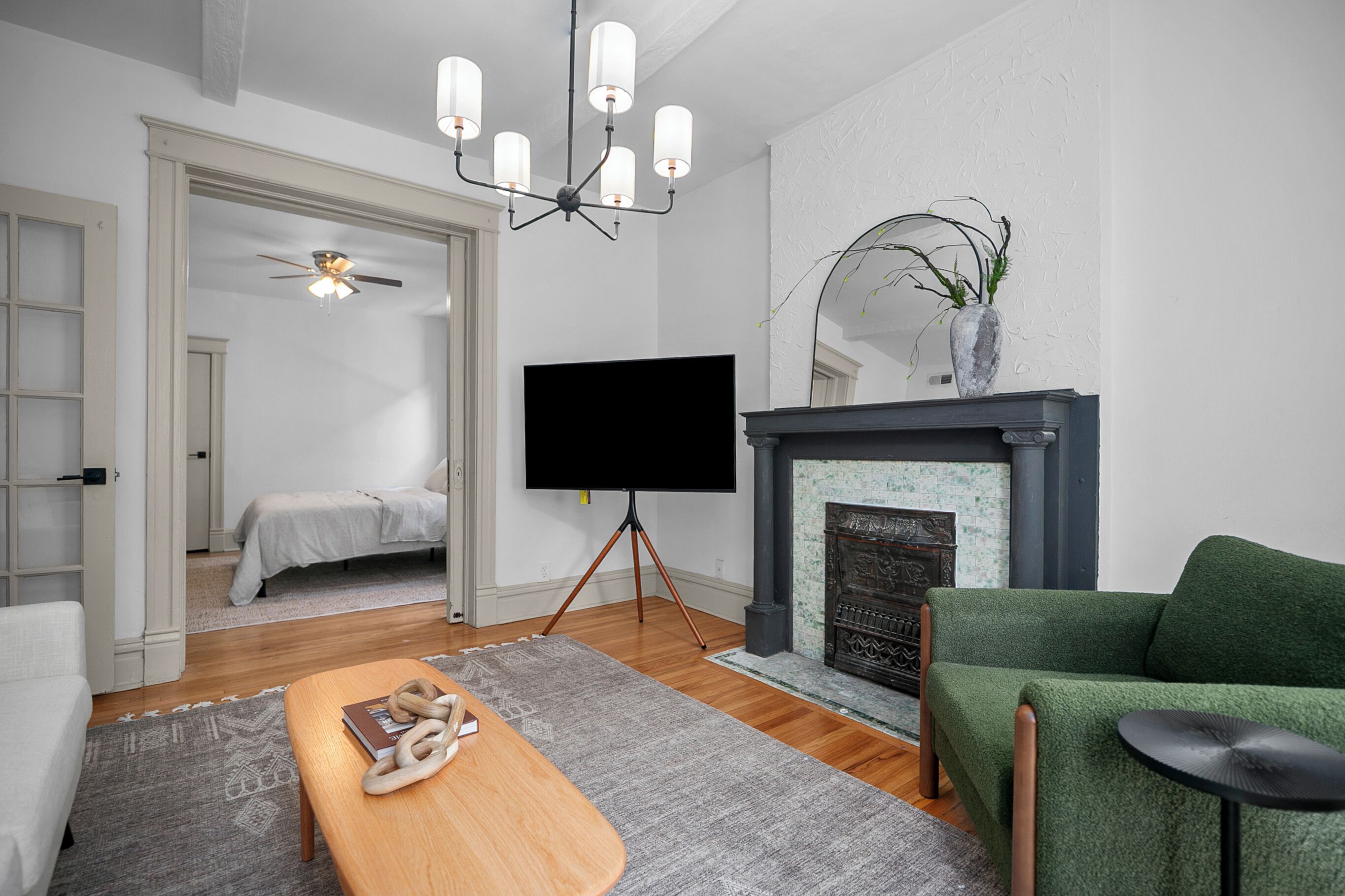 Un salon moderne avec une cheminée, un téléviseur à écran plat posé sur un trépied, un canapé vert et une table basse en bois.