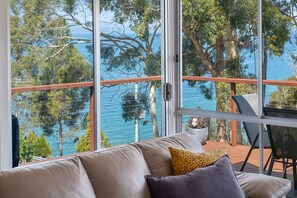 A balcony with a view of the sea, a sofa with cushions, and a table with a chair.
