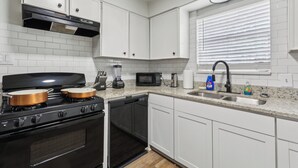 A modern kitchen with white cabinets, a stainless steel stove, a microwave, and a sink. - Four Seasons Retreat (Little Rock)
