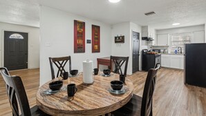 A dining area with a round table, chairs, and a kitchen in the background. - Four Seasons Retreat (Little Rock)