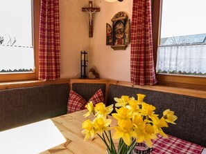 A room with a wooden bench, a table with a vase of yellow flowers, a crucifix, and a religious painting on the wall.