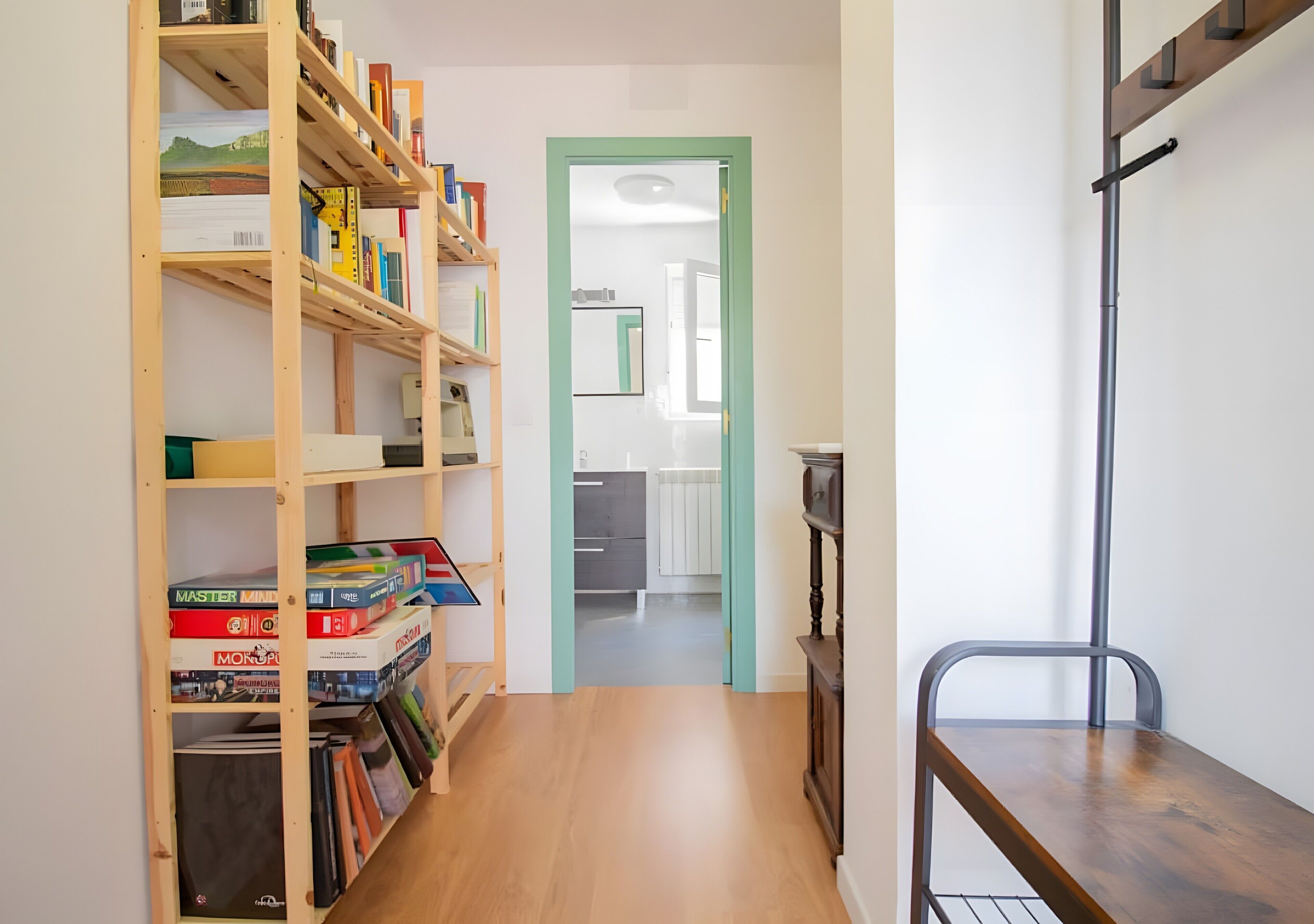 A hallway with a wooden bookshelf, a metal bench, and a green door leading to a room.