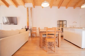 A cozy living room with a sofa, wooden dining table, chairs, and a kitchen area with a sink and cabinets.