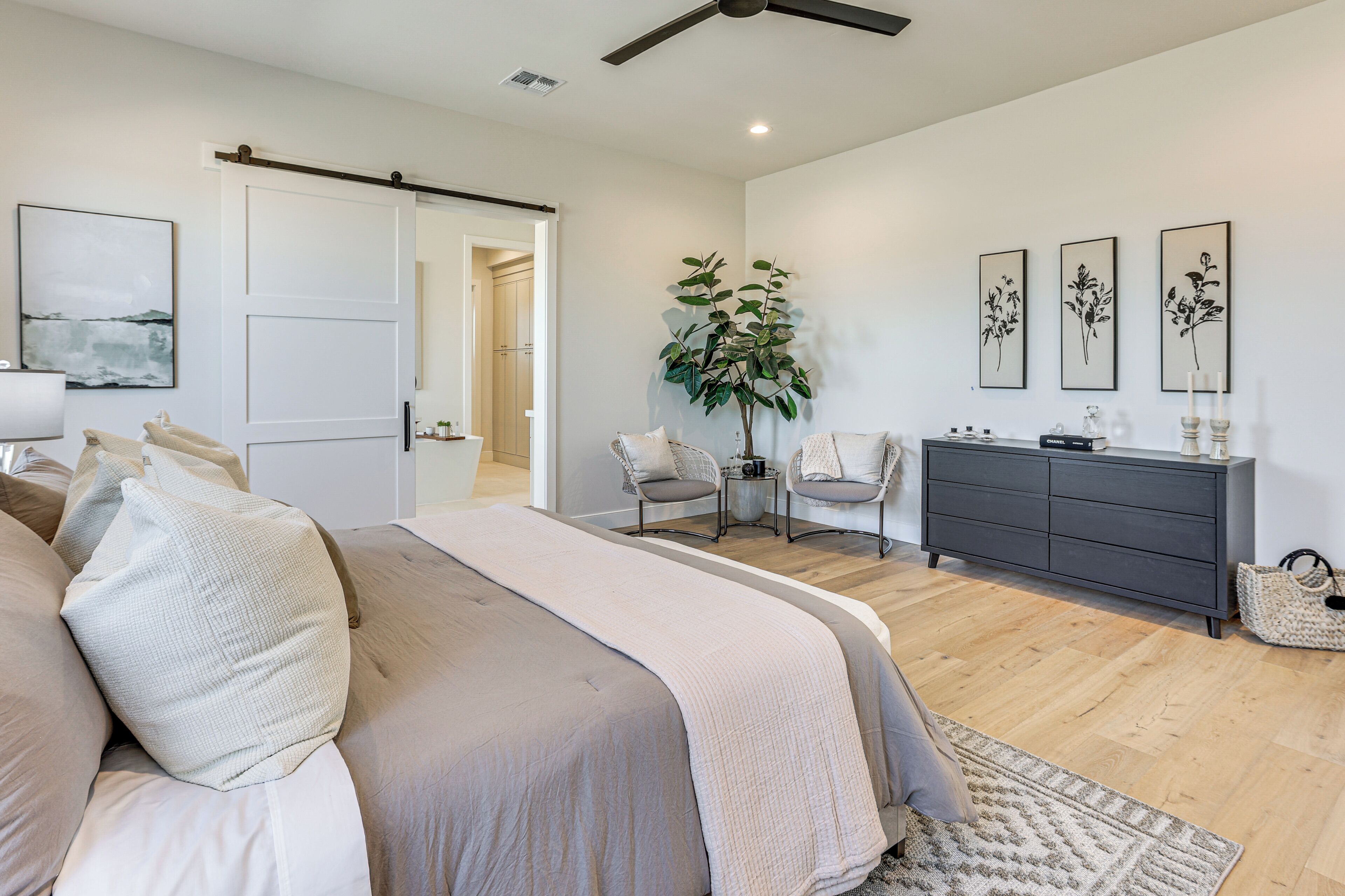 A bedroom with a bed, a dresser, a plant, and artwork on the wall.