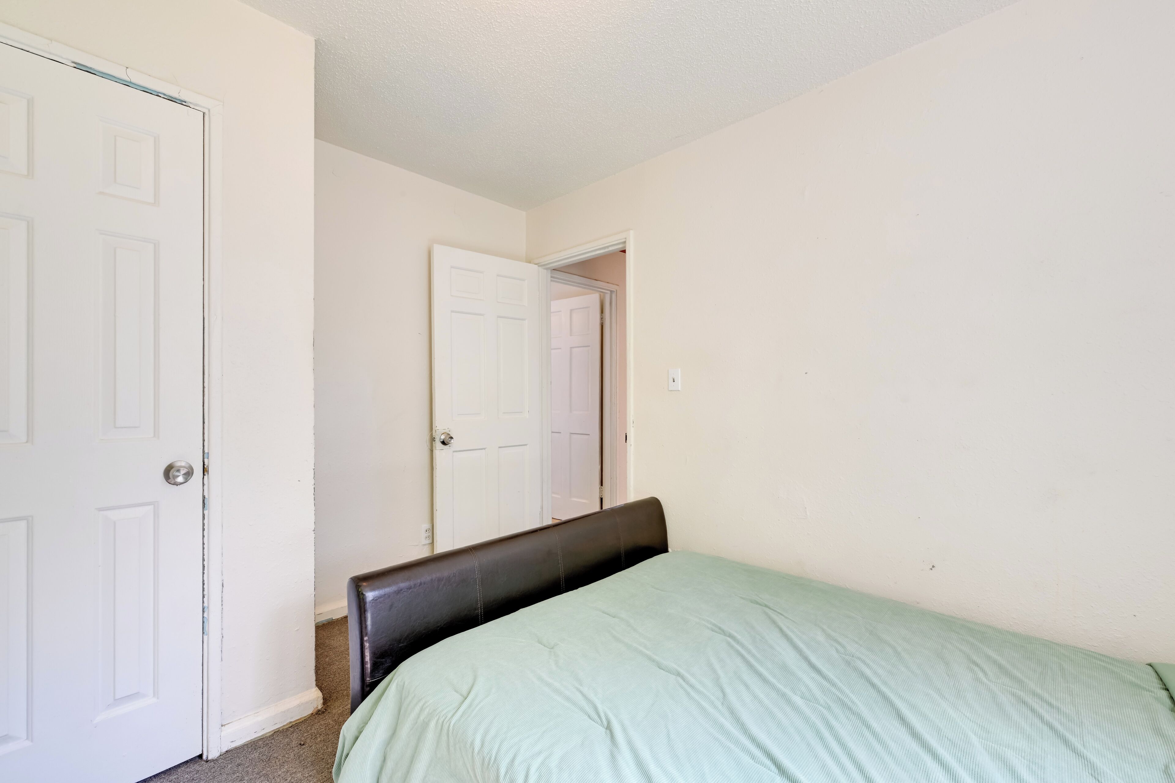 A bedroom with a single bed, a white door, and a mirror on the wall.