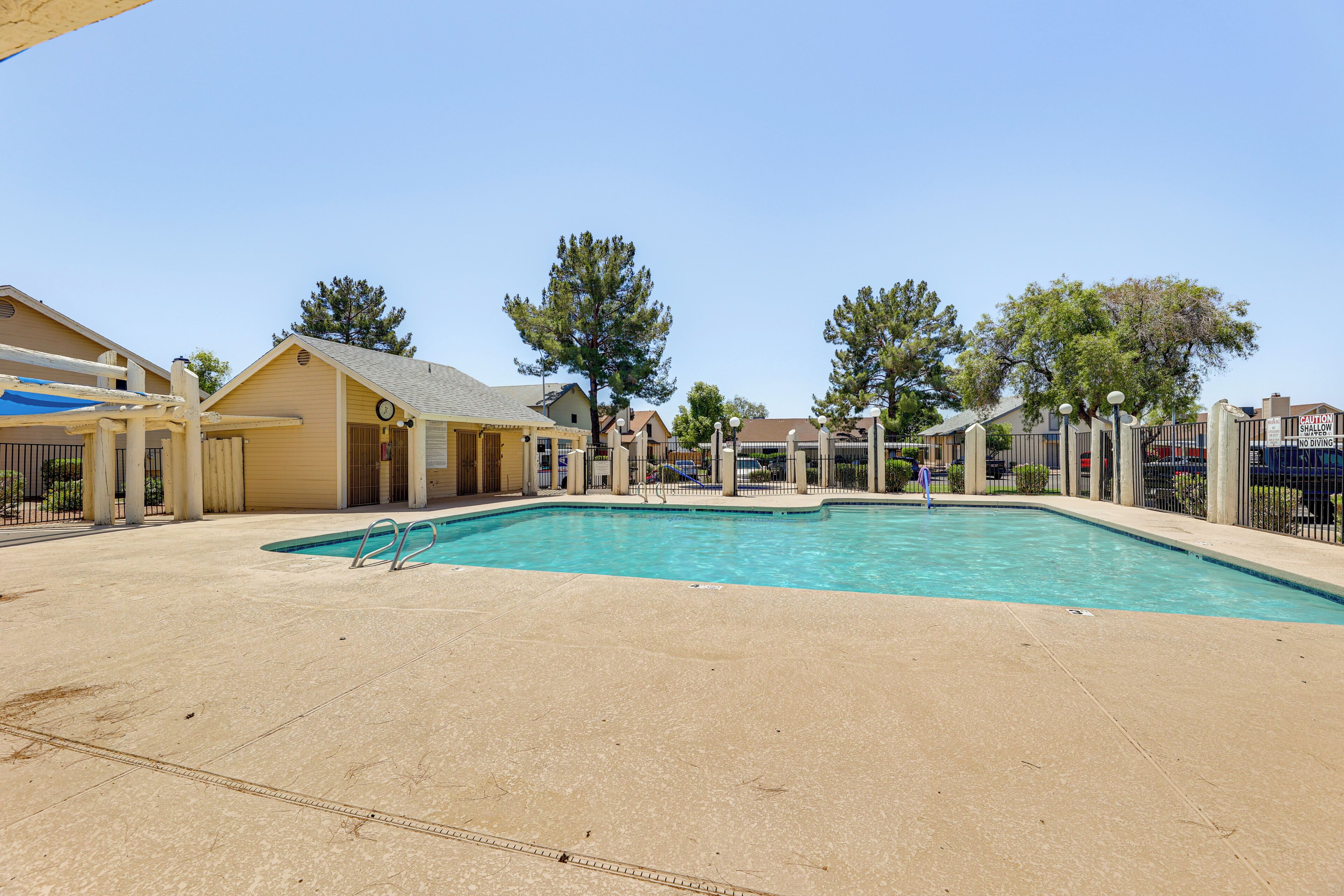 A swimming pool area with a clear blue pool, a covered seating area, and a fenced perimeter.