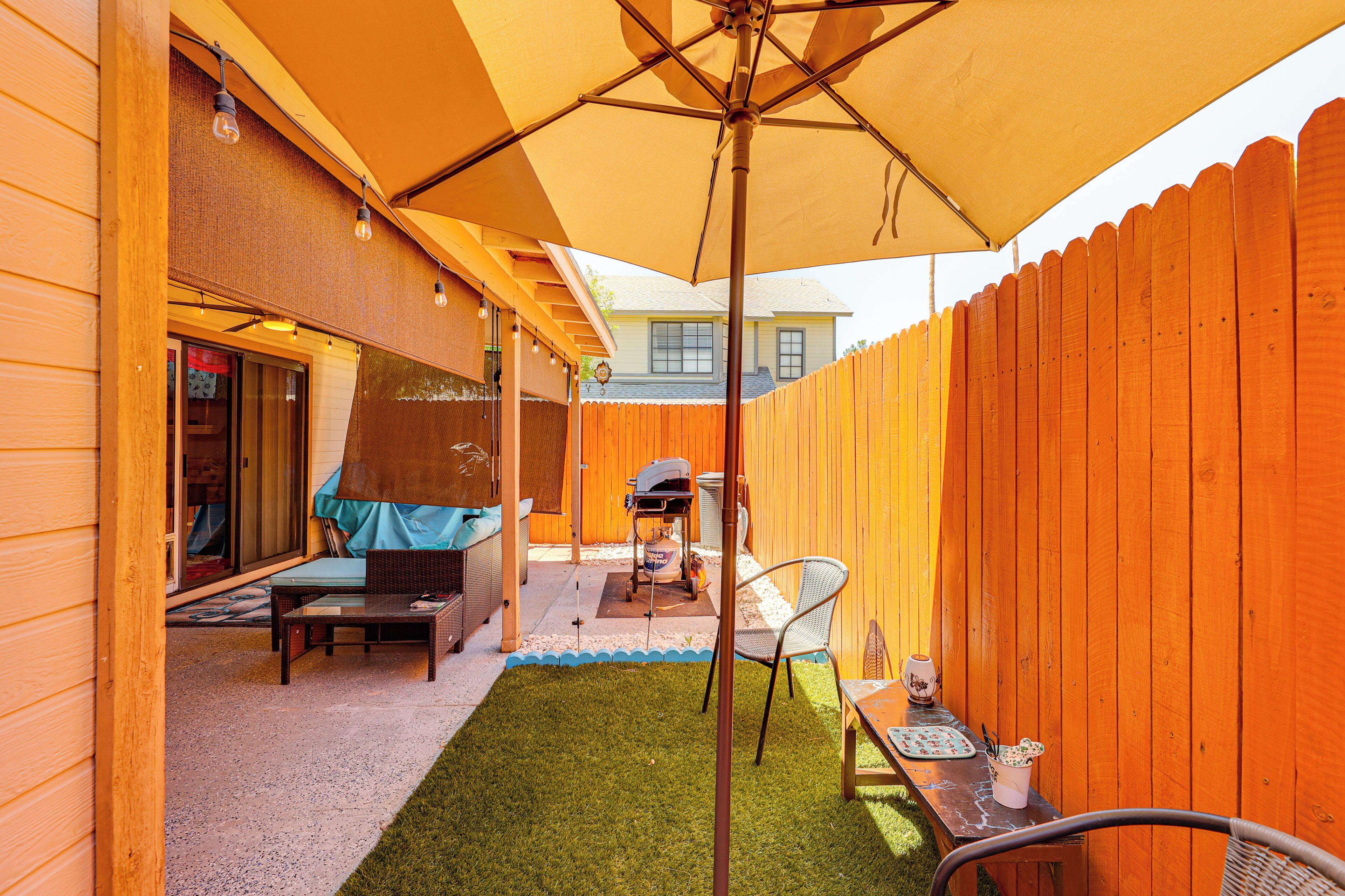 A patio with a wooden fence, a table with chairs, and a grill area.