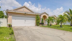 A residential house with a large garage, a well-maintained lawn, and a clear sky. - Screened Patio & Hot Tub: Port St Lucie Home! (Port Saint Lucie)