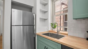 Eine moderne Küche mit einem Edelstahl-Kühlschrank, einer Holz Arbeitsplatte und einem Fenster mit Blick auf ein Backsteingebäude.